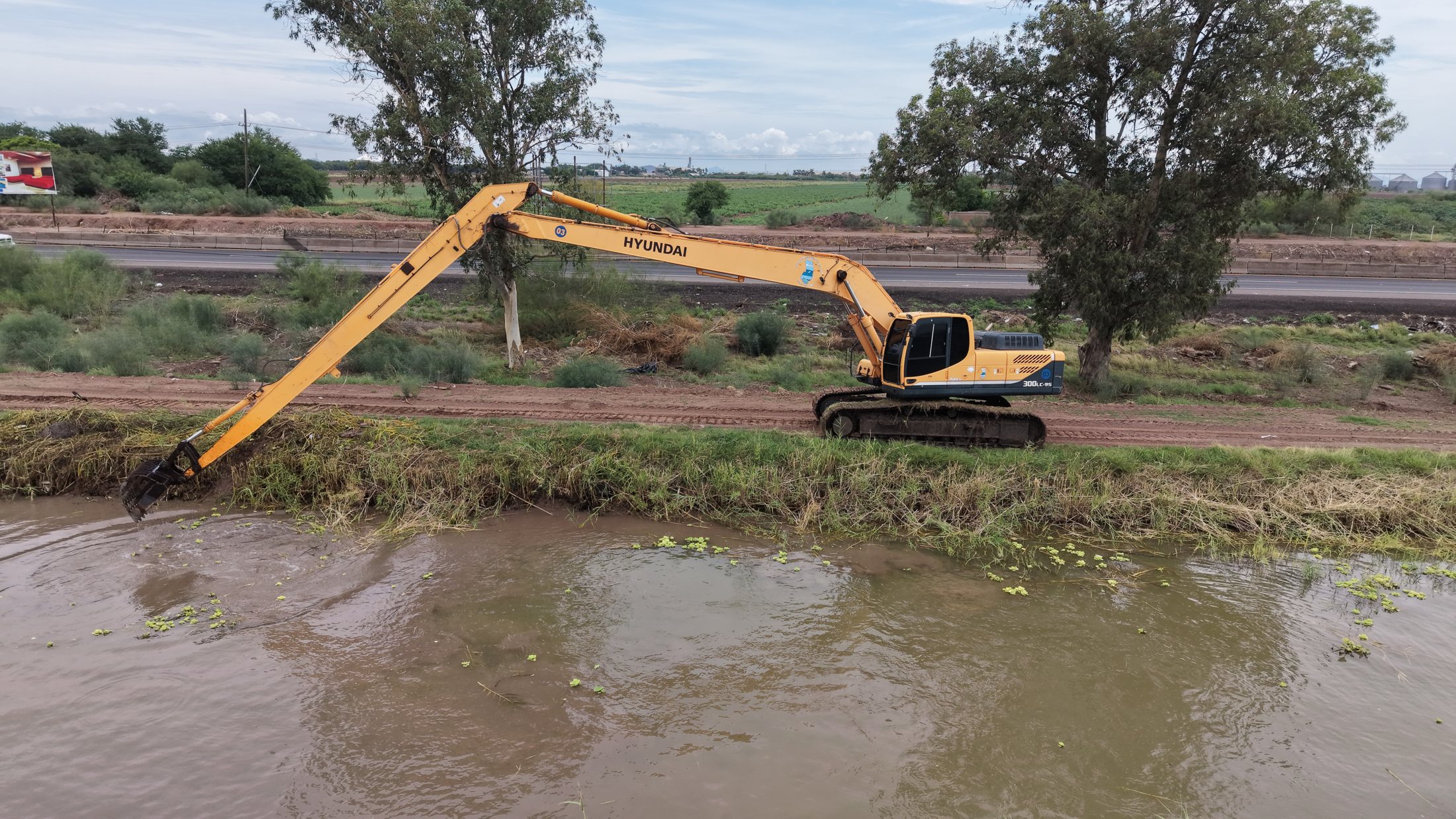 Excavadora trabajando sobre canal con agua y retiro de vegetación, agosto de 2026.